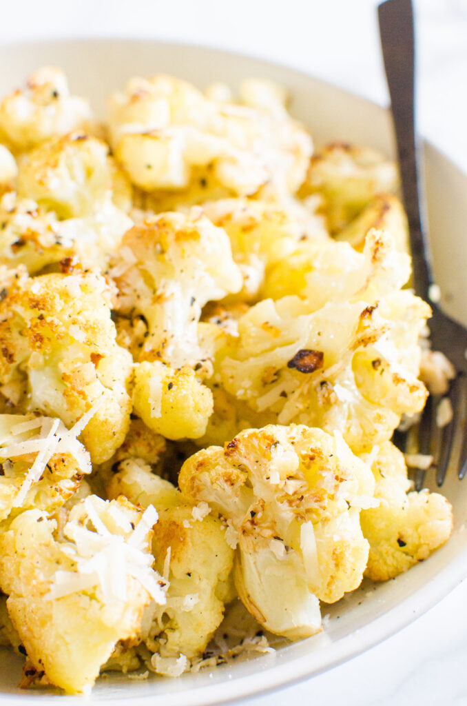 roasted cauliflower with parmesan cheese in a bowl with a fork for eating