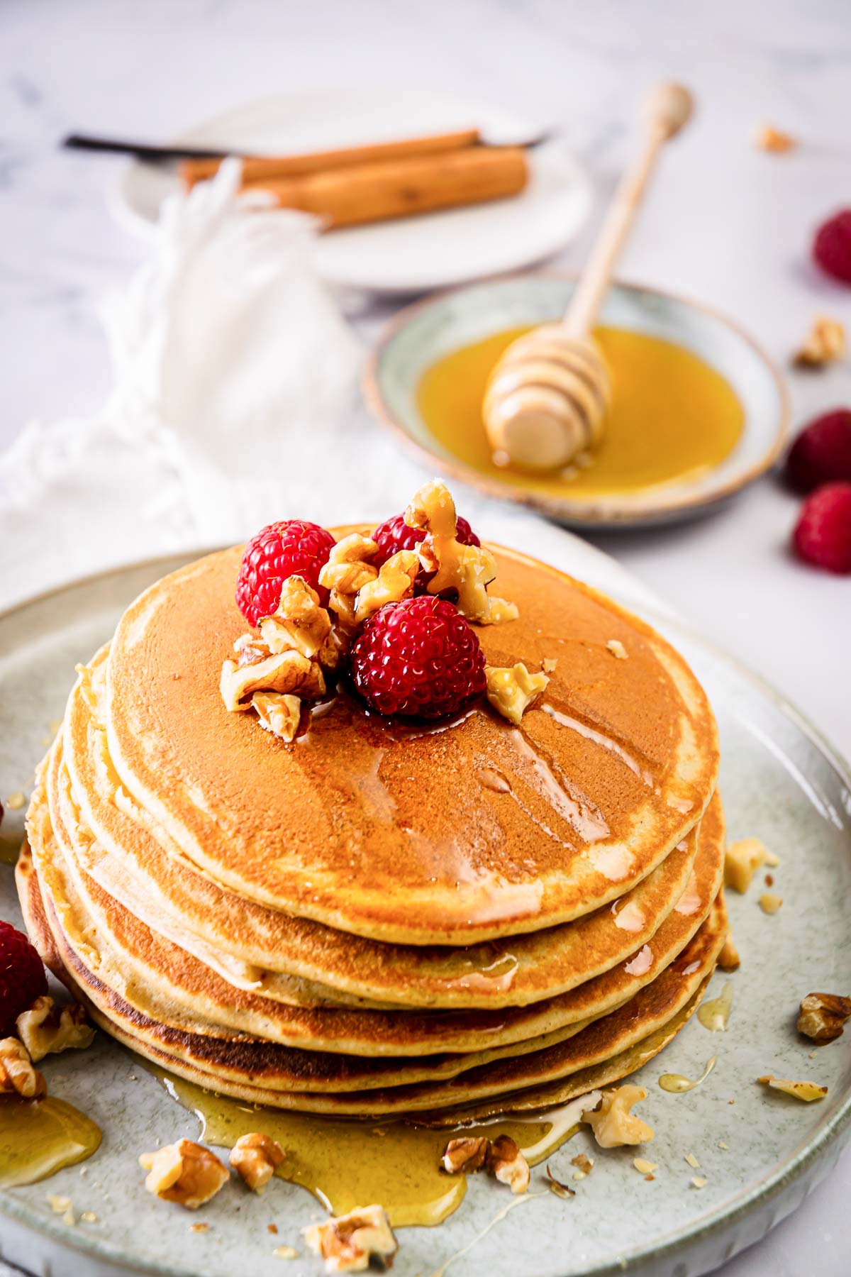 A stack of protein pancakes topped with walnuts, raspberries and honey drizzle.