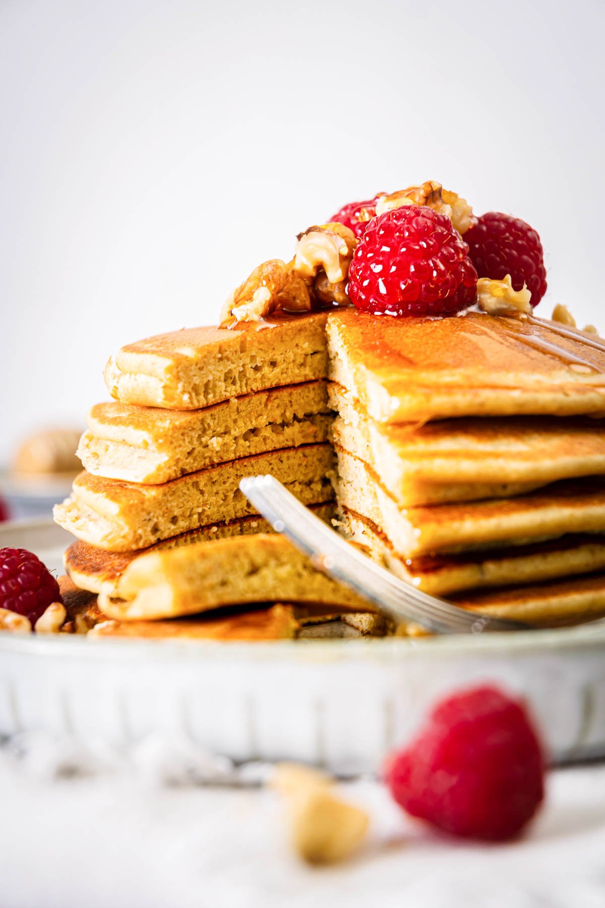 Banana protein pancakes stacked, topped with raspberries, and sliced into on a plate.