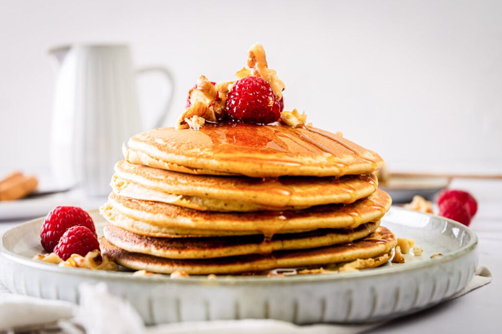 Stacked pancakes on a plate with fresh raspberries. 