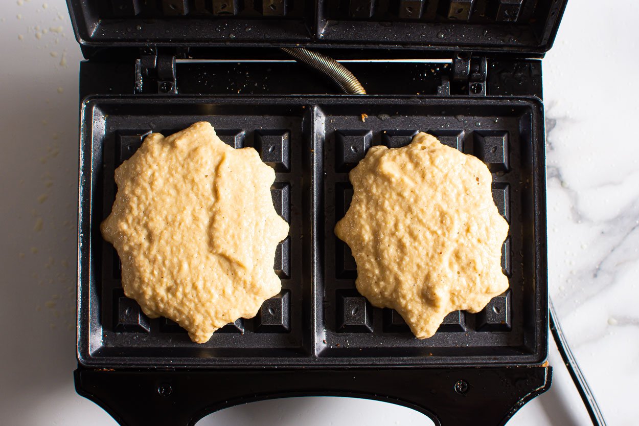 Two almond flour waffles batter on waffle iron.