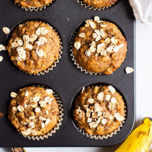 banana oatmeal muffins in a muffin pan with a banana beside the pan