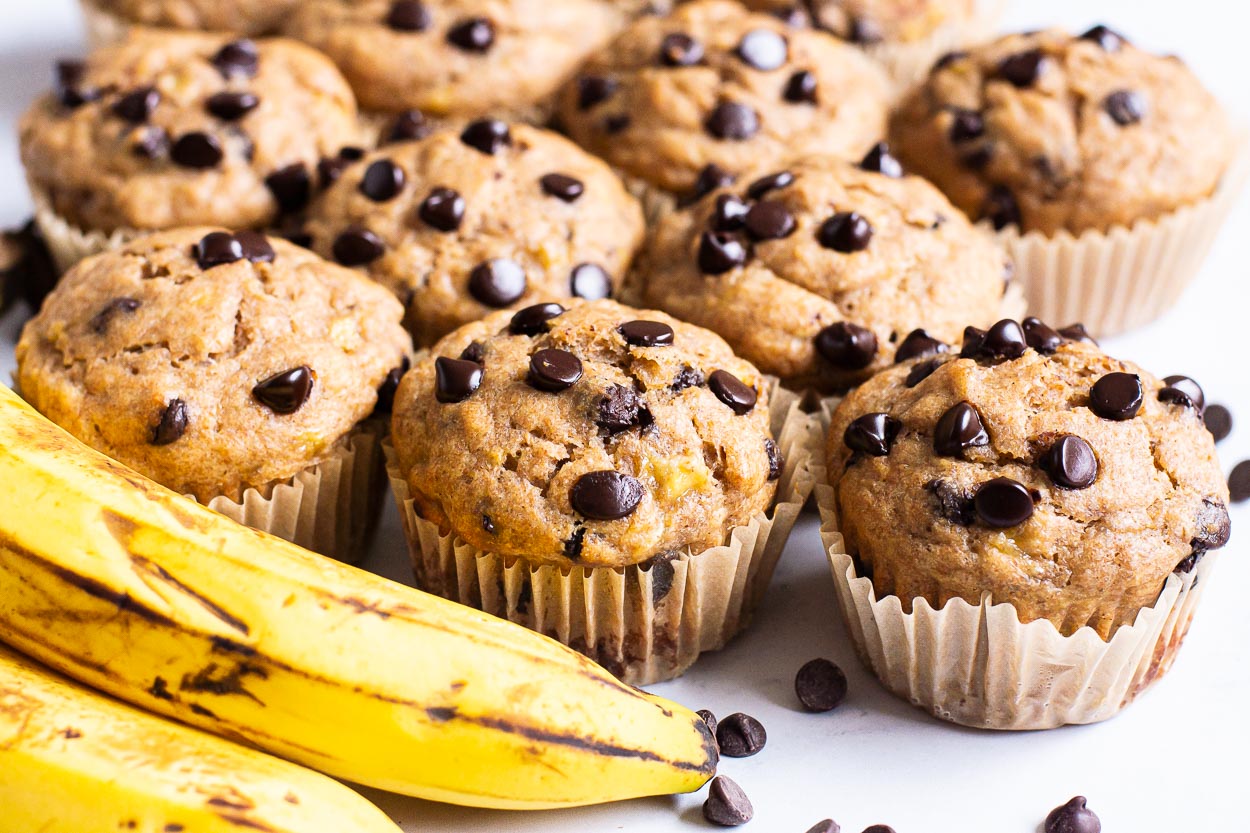 Healthy banana chocolate chip muffins with a ripe banana and chocolate chips nearby.