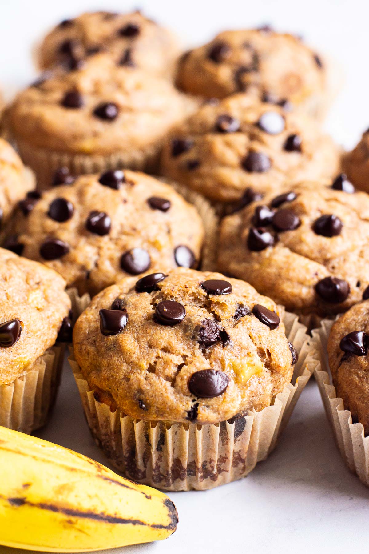 Healthy banana chocolate chip muffins in paper liners and banana nearby.