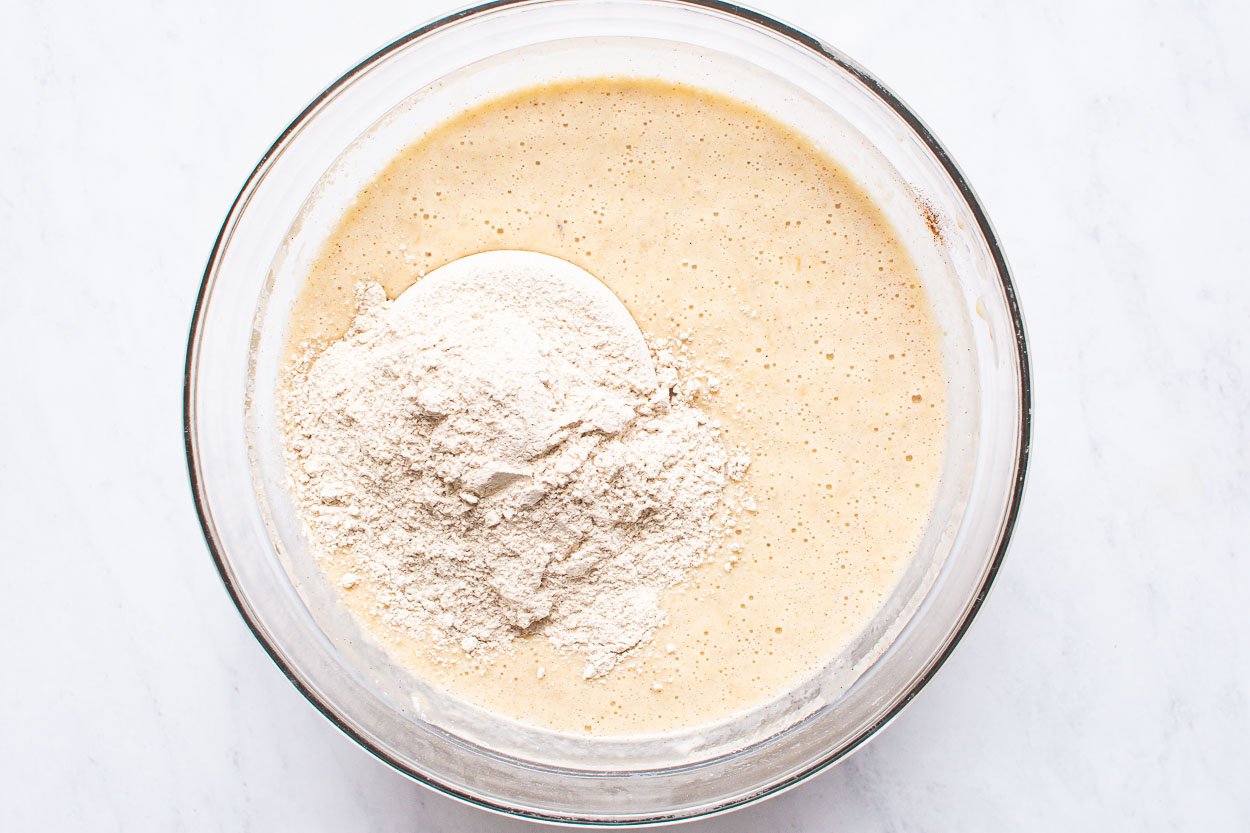 Spelt flour added to glass bowl with liquid batter.