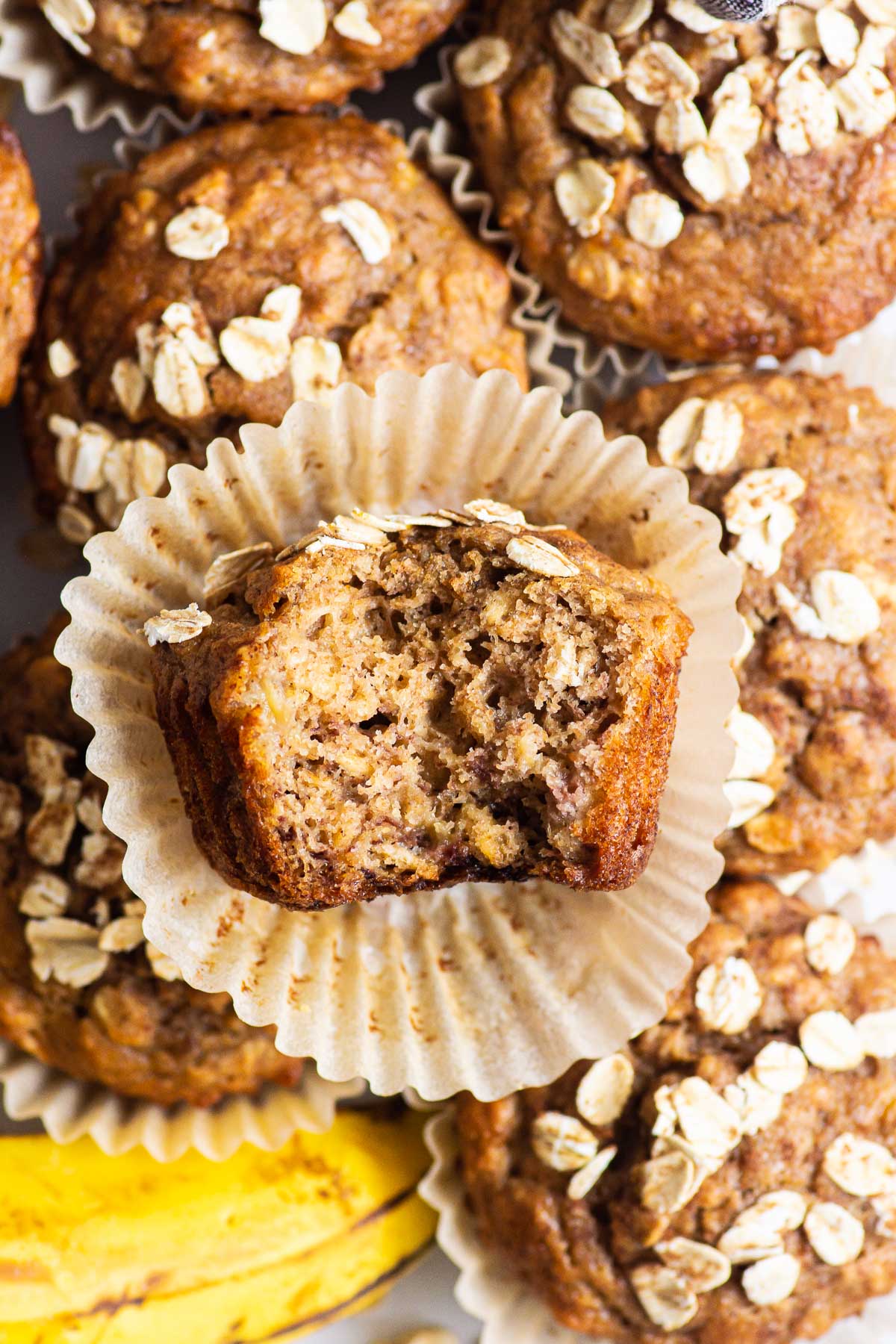 A few banana oatmeal muffins and one stacked on top that has been unwrapped and a bite taken out of.