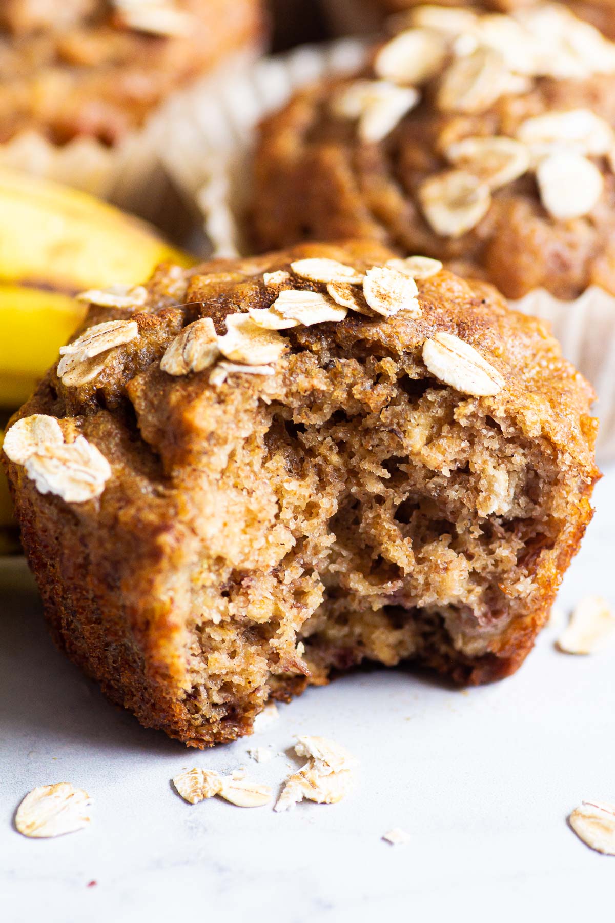 Banana oatmeal muffins with oats on top with a bite taken out of one.