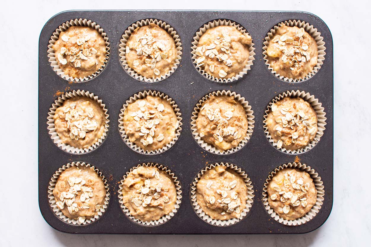 Unbaked healthy banana oatmeal muffins in paper liners in a muffin tin.