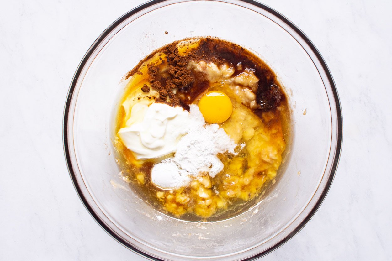 Egg, yogurt, oil, maple syrup and baking essentials in glass bowl.