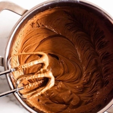 Chocolate frosting in a saucepan with beaters resting on the pan..