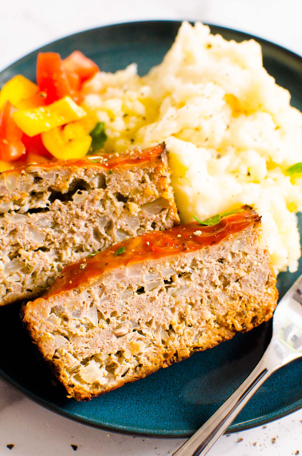 turkey meatloaf on plate for serving with mashed potatoes and bell peppers