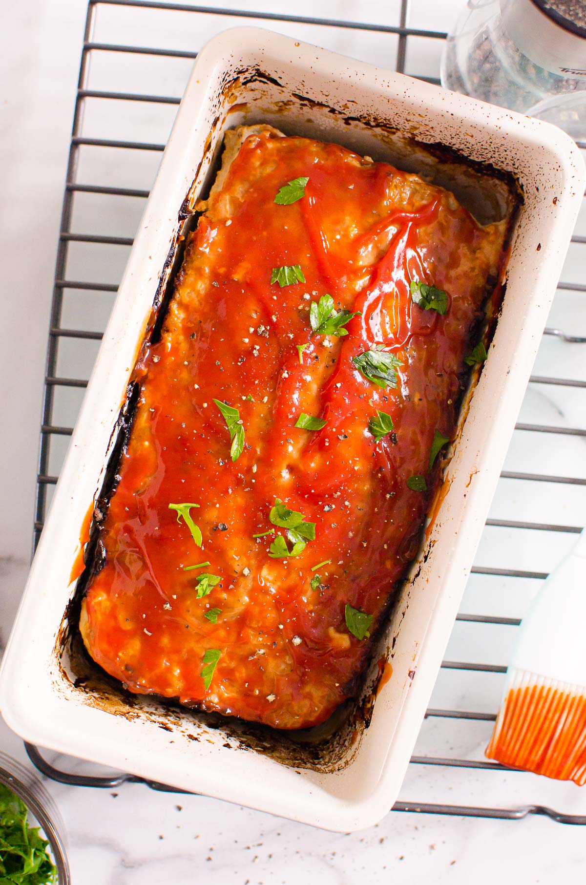 Turkey meatloaf with ketchup glaze in a pan on top of cooling rack with a brush.