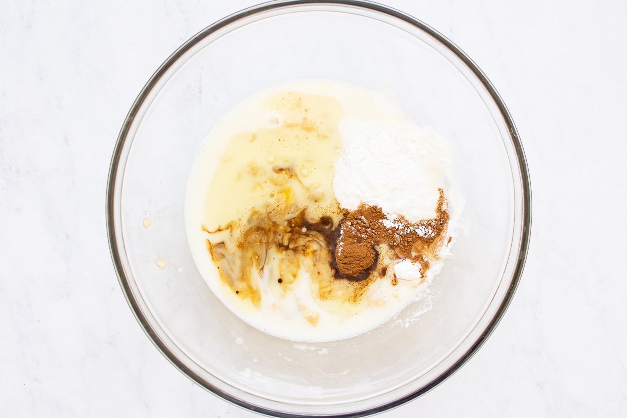 Milk, oil, maple syrup, egg, cinnamon and leavening agents in glass bowl.