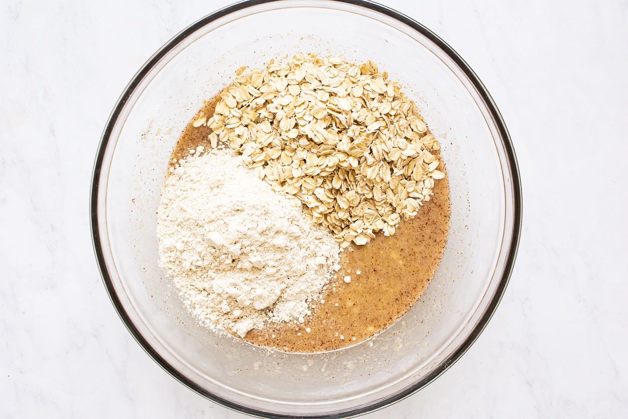 Oat flour and rolled oats added to a bowl with liquid batter.