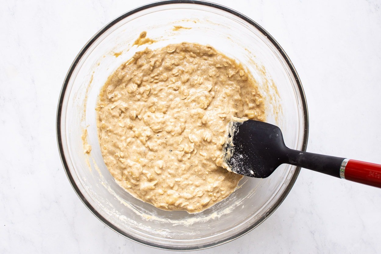Muffins batter in glass bowl with black spatula.