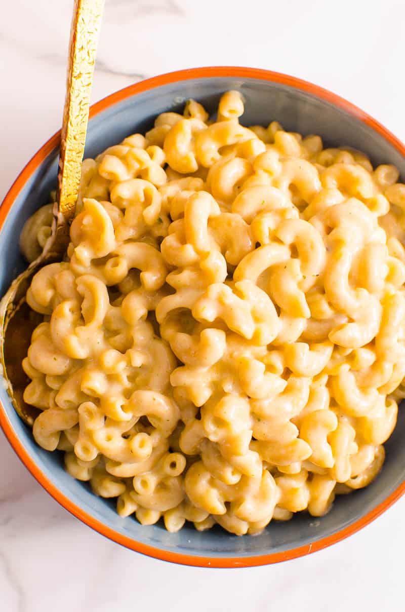Macaroni with cheese sauce in blue bowl with gold spoon.