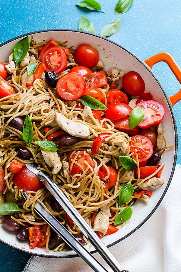 Pasta in large pot with chicken, olives, tomato and olives.