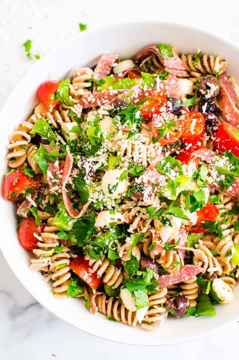 Italian pasta salad with salami and fresh herbs in white bowl.