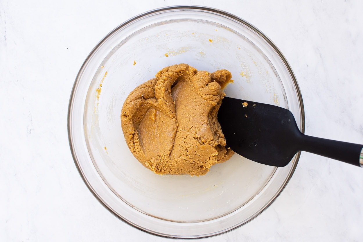 Healthy peanut butter cookie dough in glass bowl with black spatula.