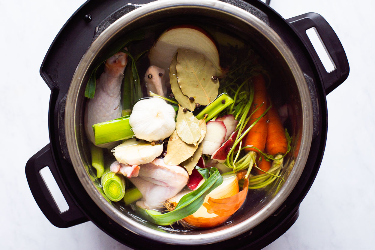 Raw vegetables and chicken carcass in pressure cooker.