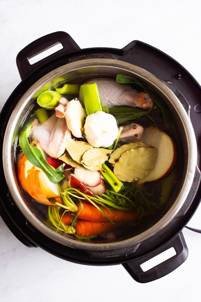 Vegetables, chicken carcass, peppercorn and bay leaves in Instant Pot. 