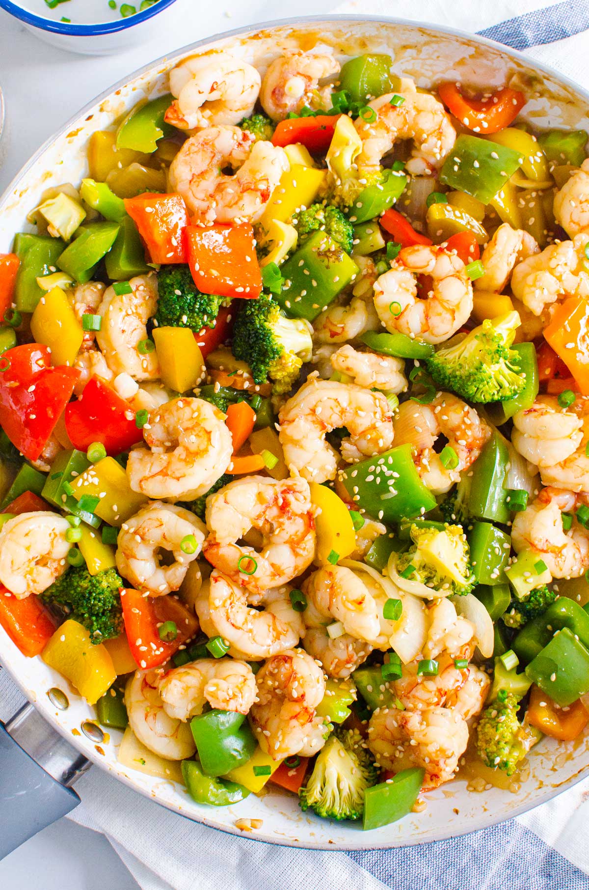 shrimp and vegetables in stir fry pan with sesame seeds and a light blue striped linen