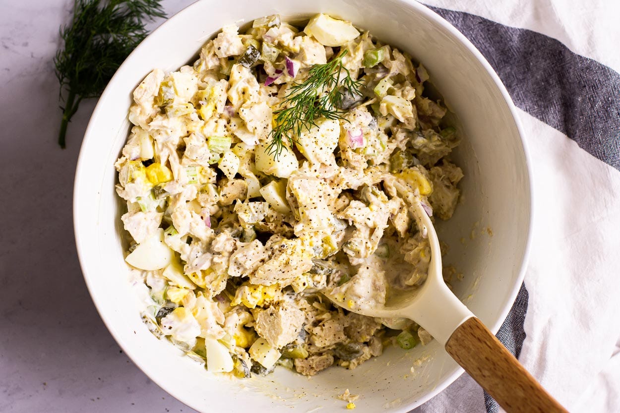 Mixed together tuna egg salad in white bowl with a spoon.