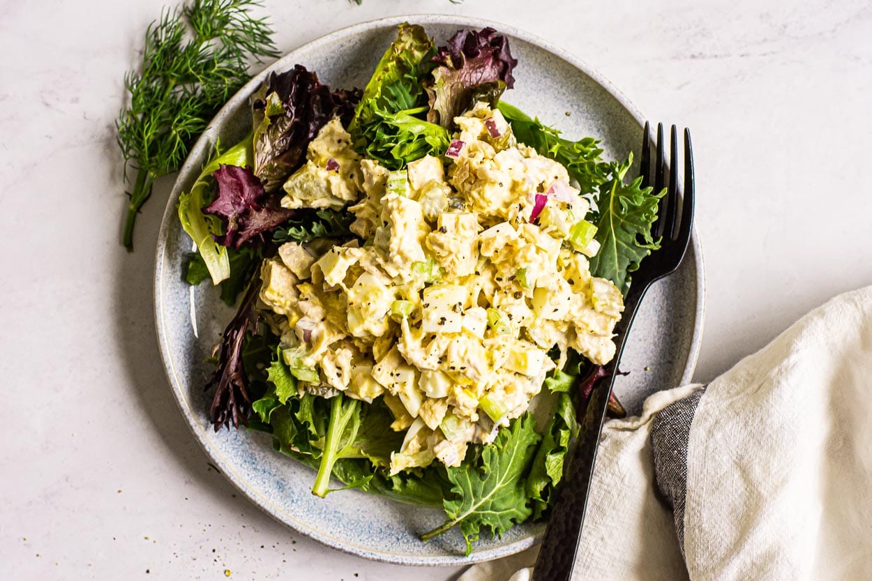 tuna salad with egg being served over mixed lettuce greens on a gray plate