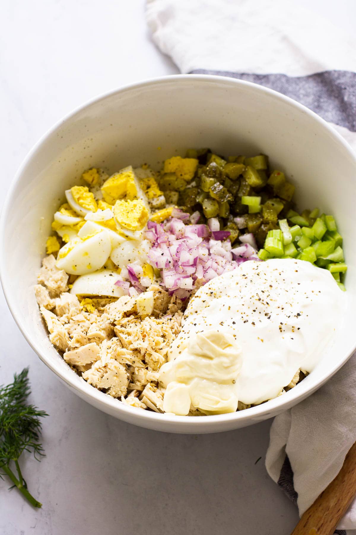 tuna egg salad ingredients in a white bowl with striped linen around bowl