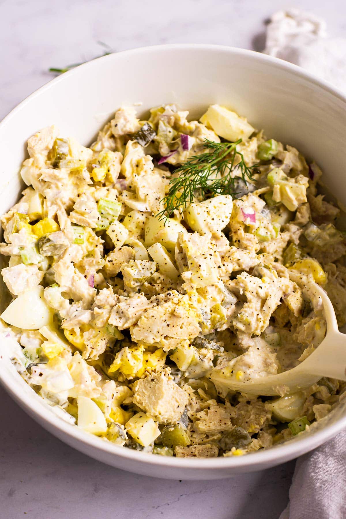 tuna egg salad in a large bowl with serving spoon and a sprig of dill