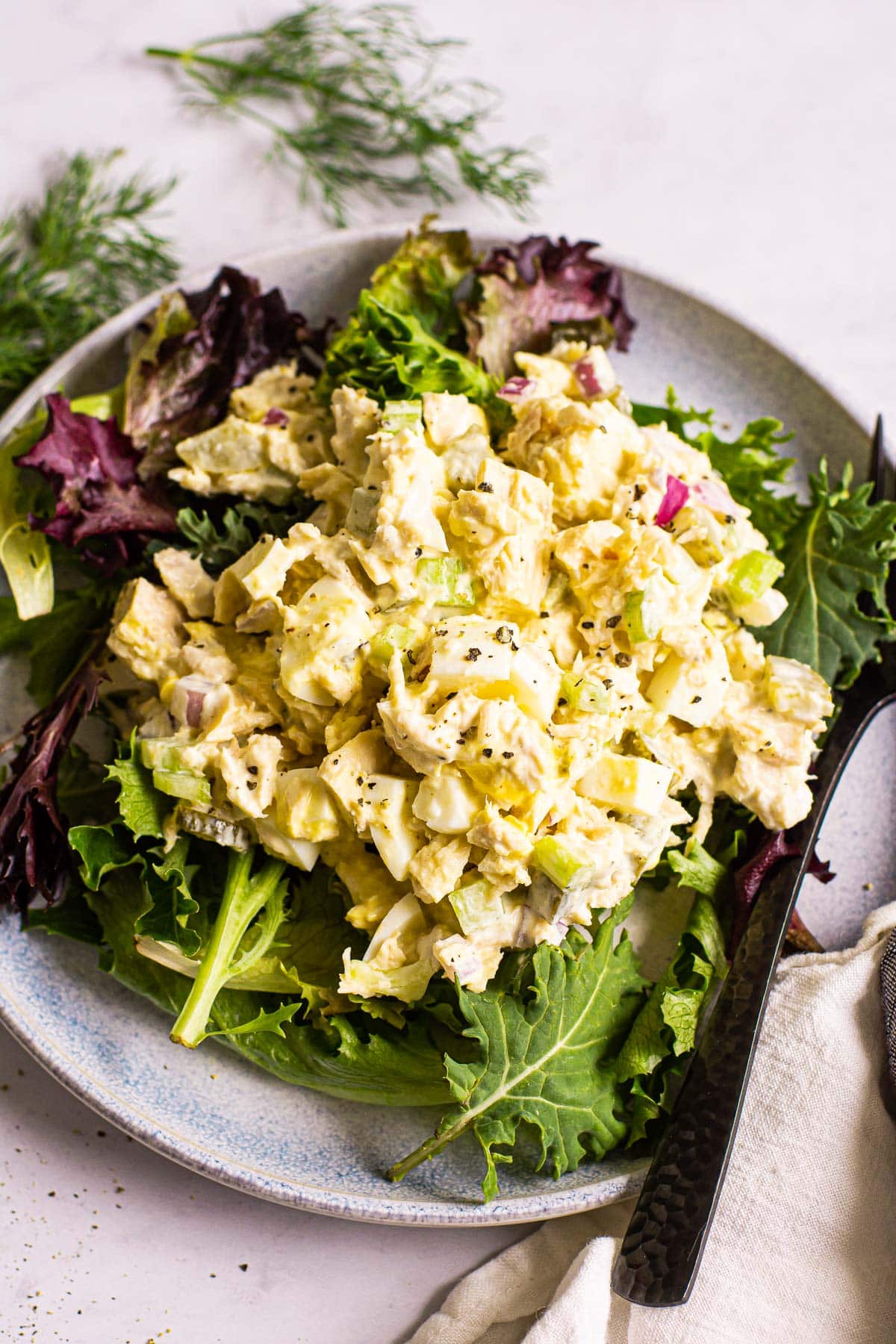 tuna and egg salad on a gray plate with fresh greens and fork