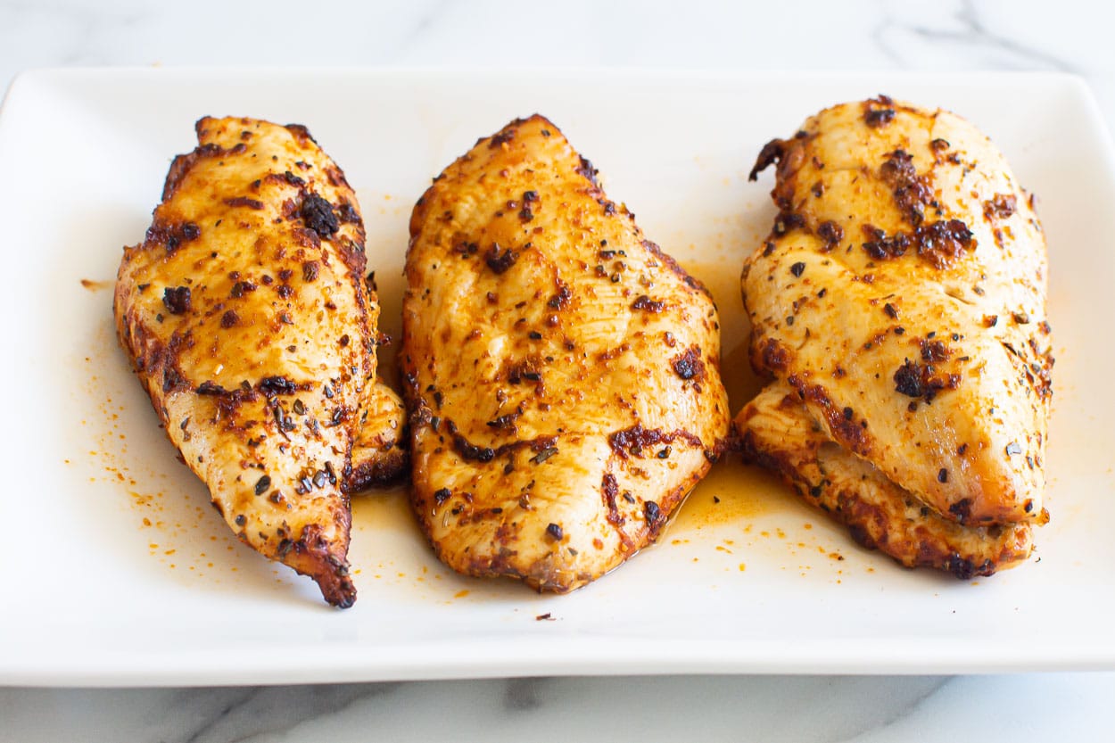 Three air fryer chicken breasts with juices on white platter.