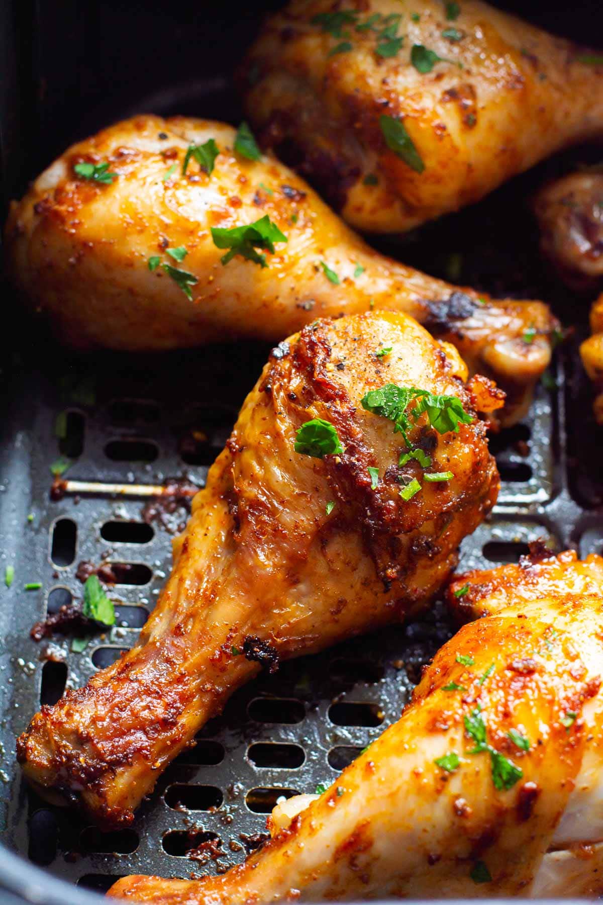 Close up of chicken legs in air fryer with garnish.