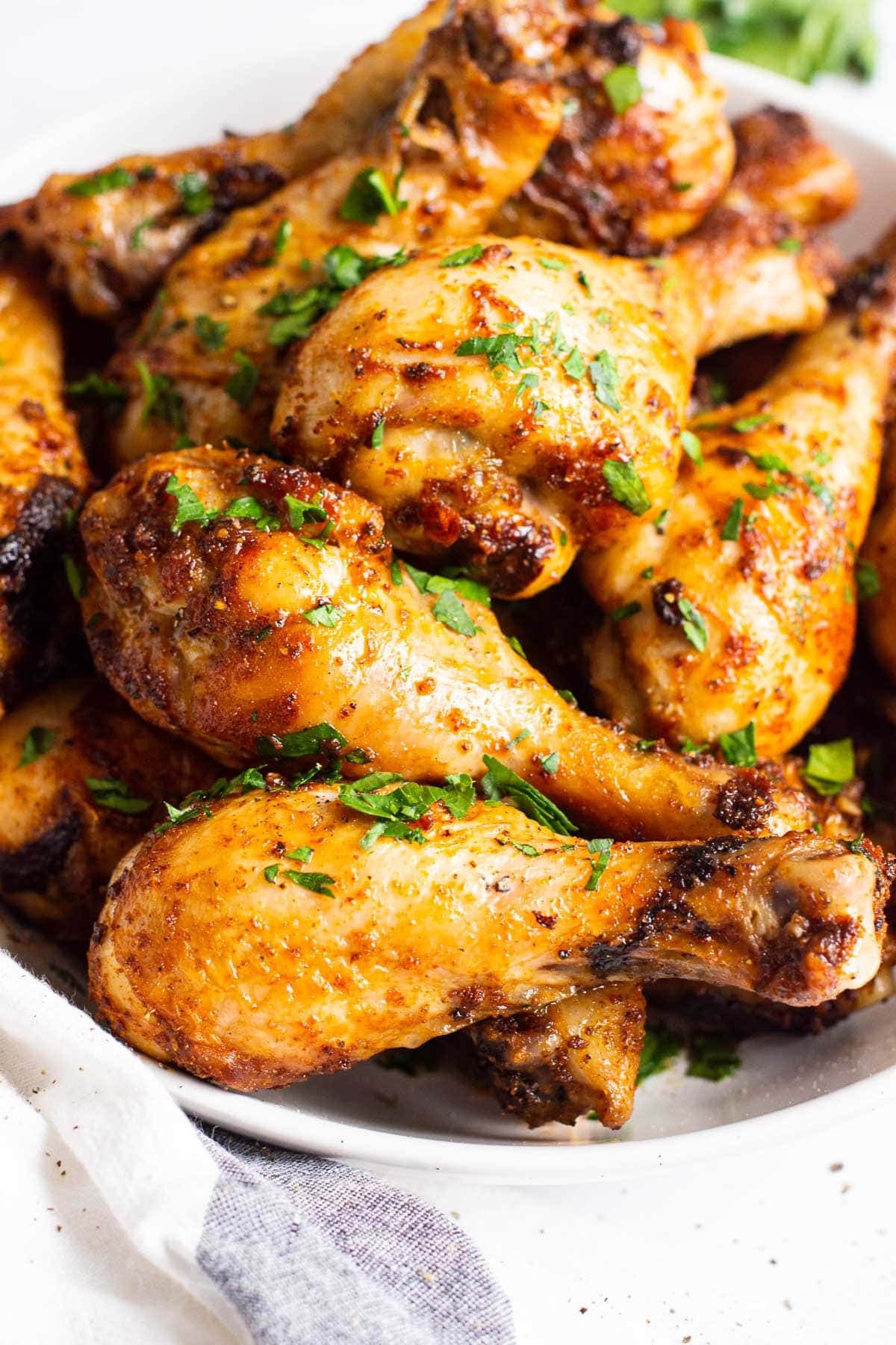 Air fryer chicken legs with green herb garnish on serving plate with a gray striped linen.