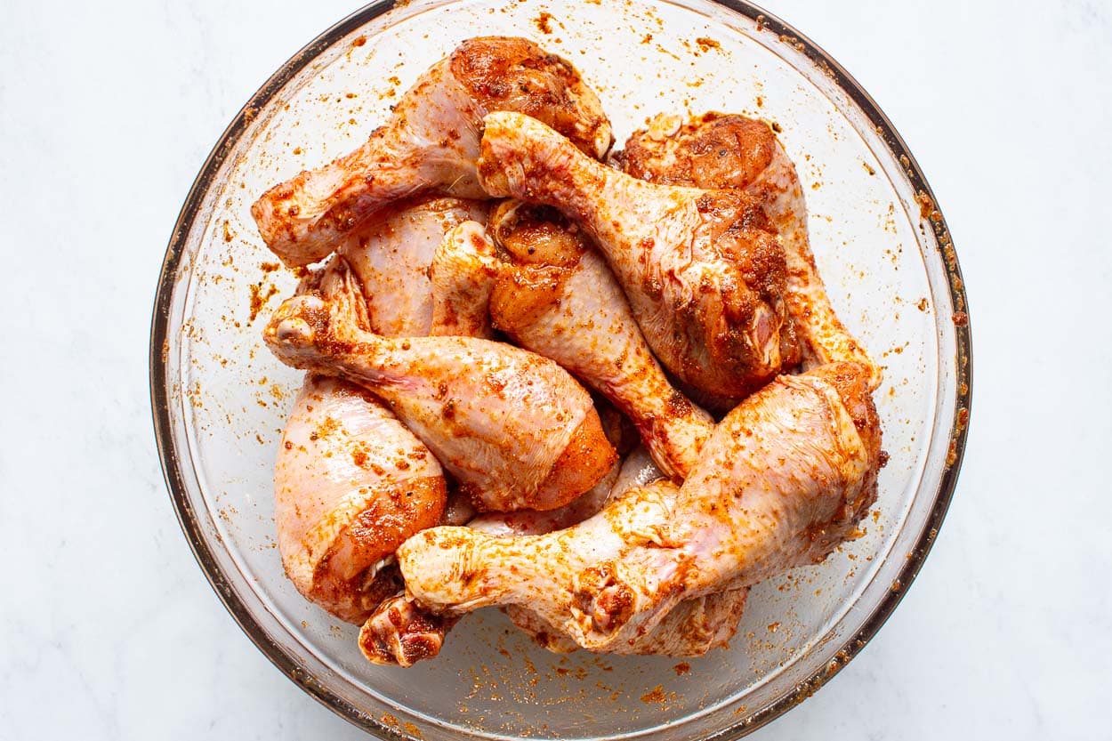 Chicken drumsticks with seasonings in a glass bowl.