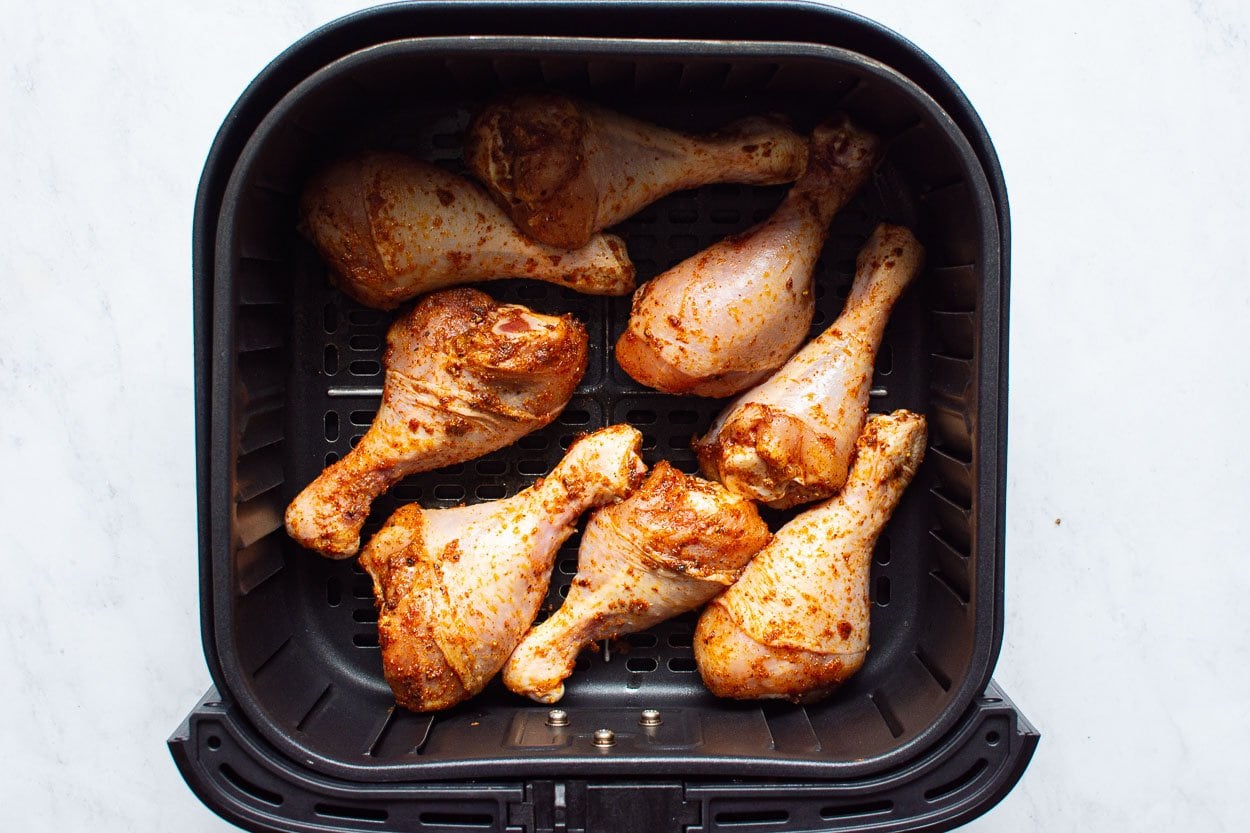 Raw chicken legs in air fryer basket.