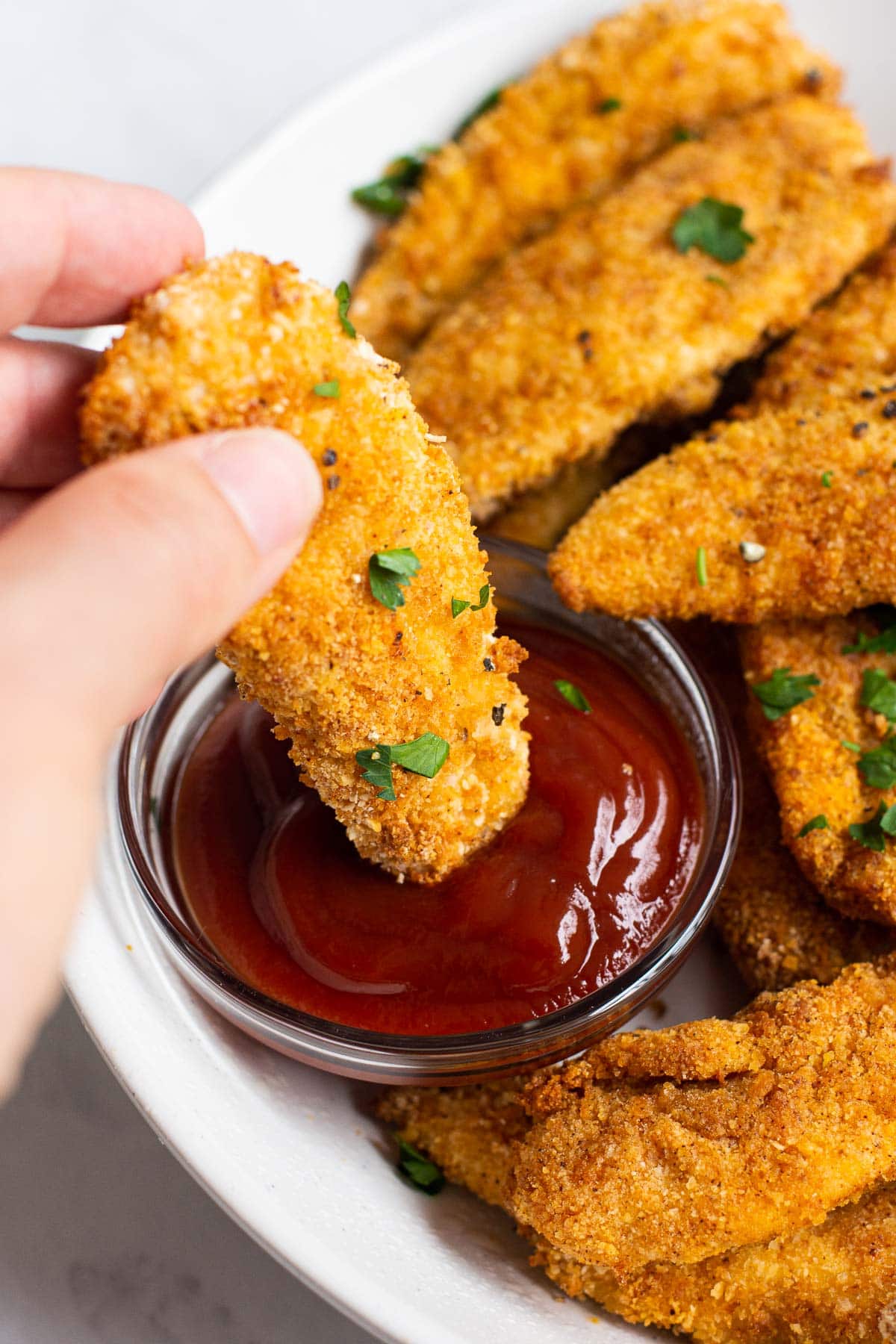 Dipping air fryer chicken tenders into ketchup.