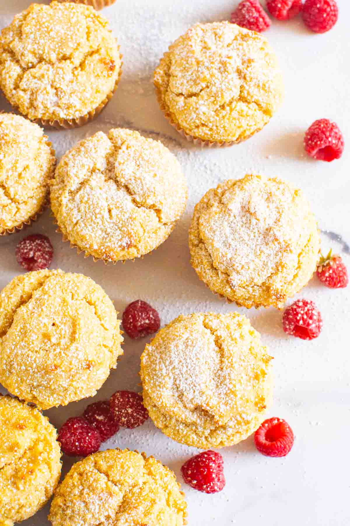 Looking down at almond flour yogurt muffins dusted with icing sugar and raspberries around them.
