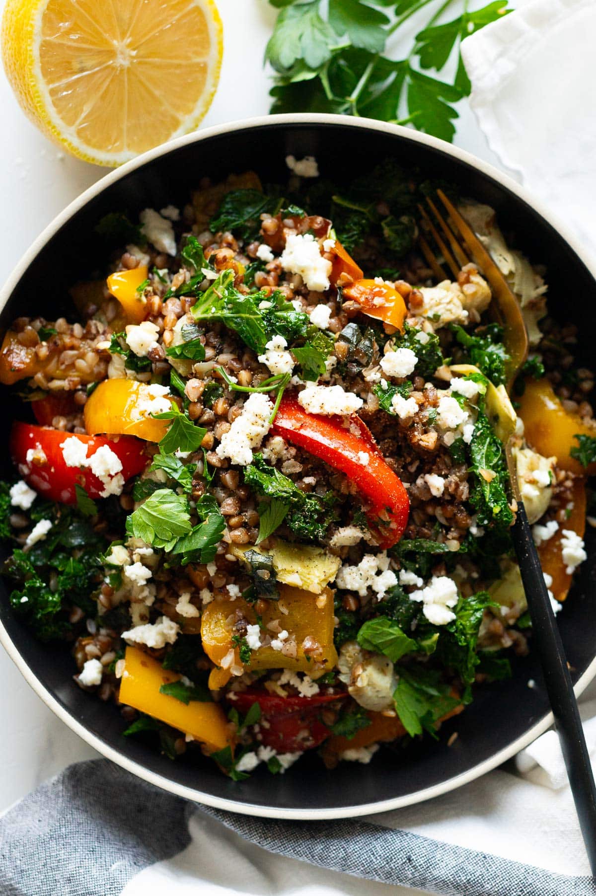 Buckwheat stir fry served in a bowl with a fork. Parsley, lemon and towel on a counter.