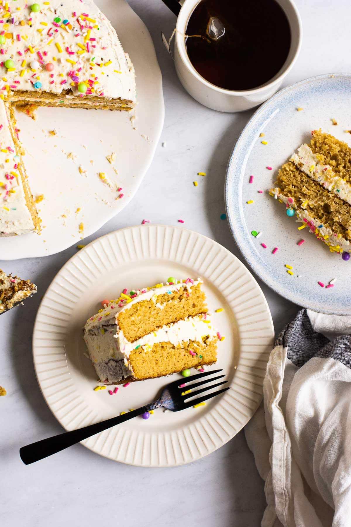 Two slices of healthy birthday cake on plates with a cup of tea and cake.