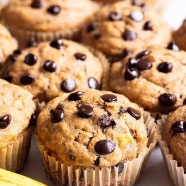 Healthy banana chocolate chip muffins with a banana in front of muffins.