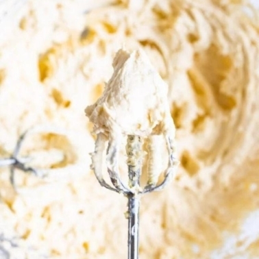 Healthy buttercream frosting on an electric mixer beater being held over the bowl.