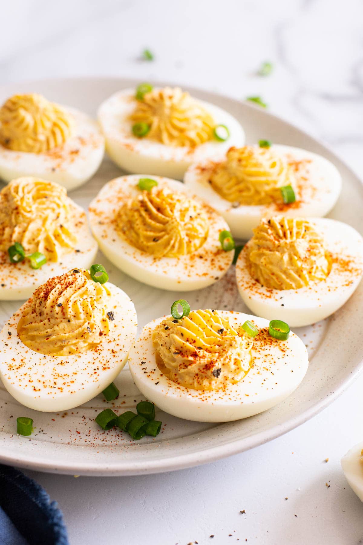 Close up of healthier deviled eggs garnished with paprika on a white plate.