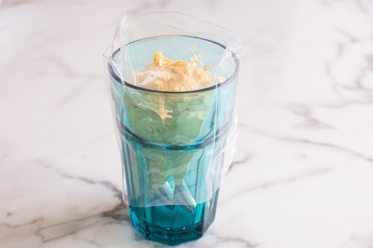 Filled piping bag with egg mixture standing in blue glass.