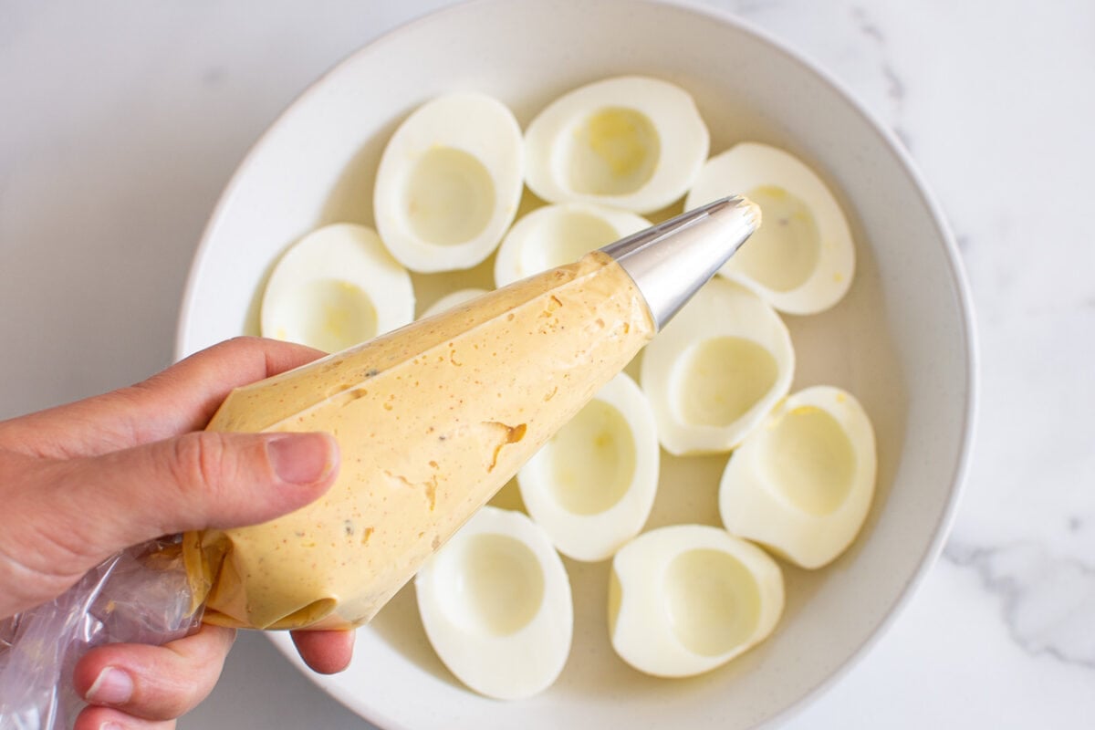 Healthy deviled egg filling in piping bag with egg whites on a plate.