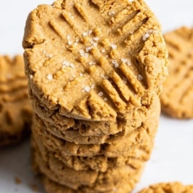 A stack of healthy peanut butter cookies with flaky salt on the top one.