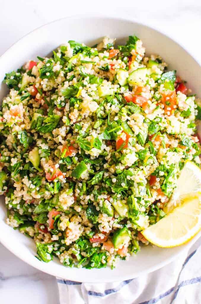 Tabbouleh quinoa salad with lemon slices in white bowl.