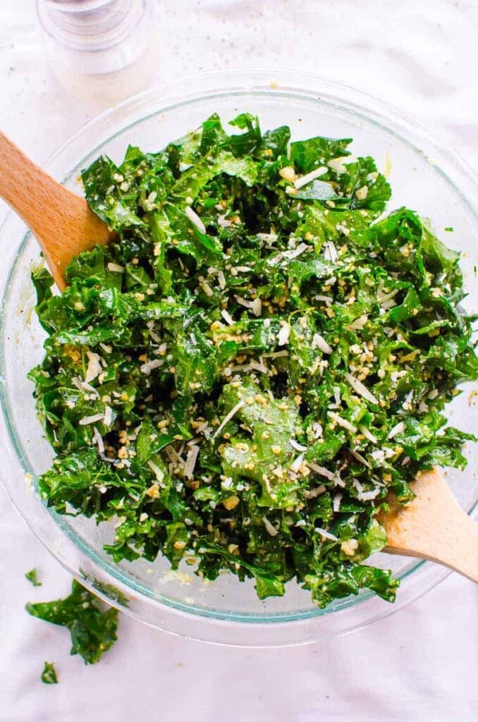 Lemon kale salad with parmesan in glass bowl and wooden spoons.
