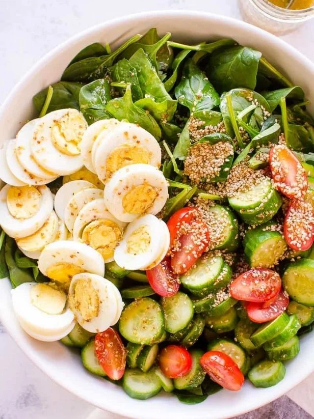 Healthy spinach salad with egg, tomato, cucumber and sesame seeds.