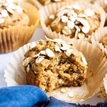 Healthy oatmeal muffin unwrapped and a bite missing with blue linen in foreground.